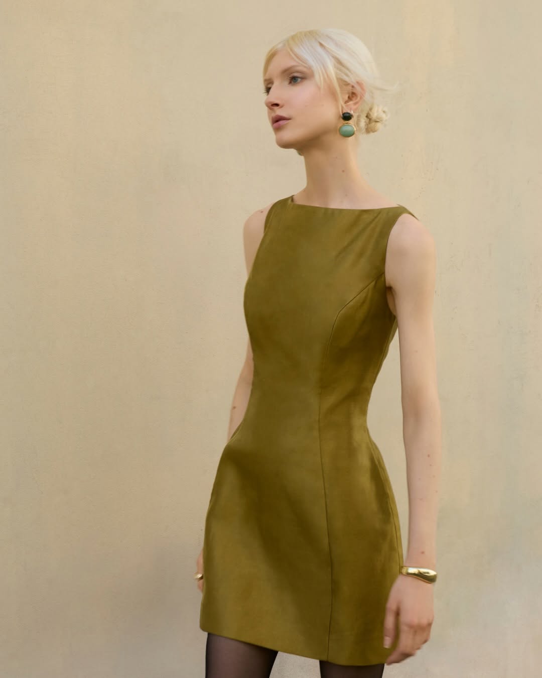 Model wearing an olive green, sleeveless mini dress with a boat neckline and structured fit.