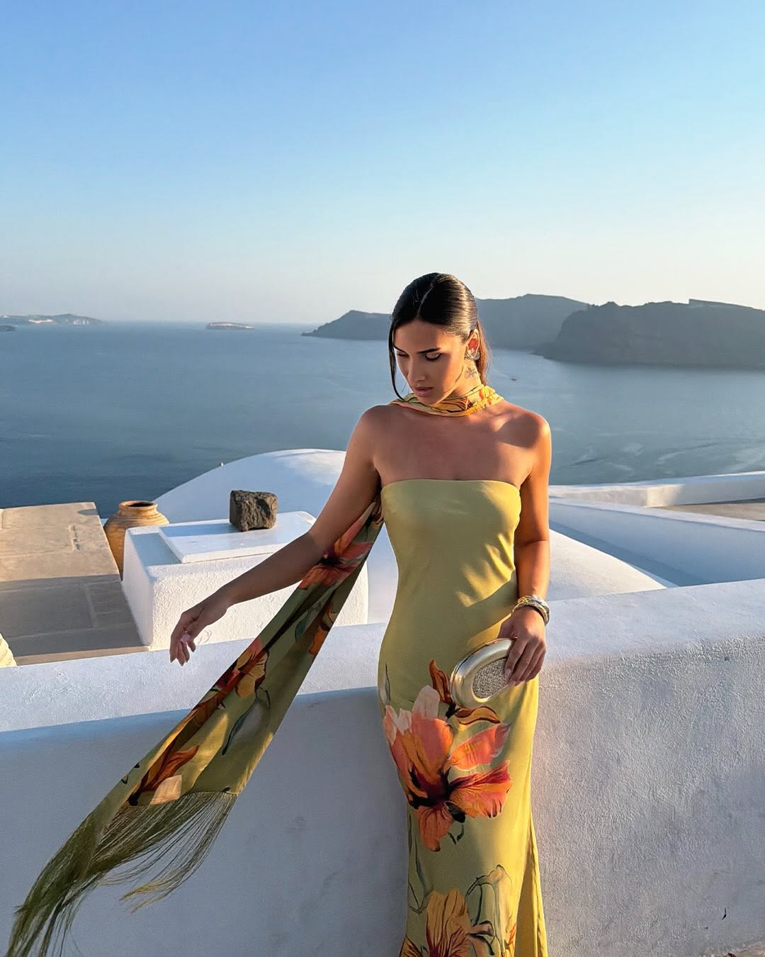 Model wearing an olive green strapless maxi dress with orange floral print and a matching long scarf.