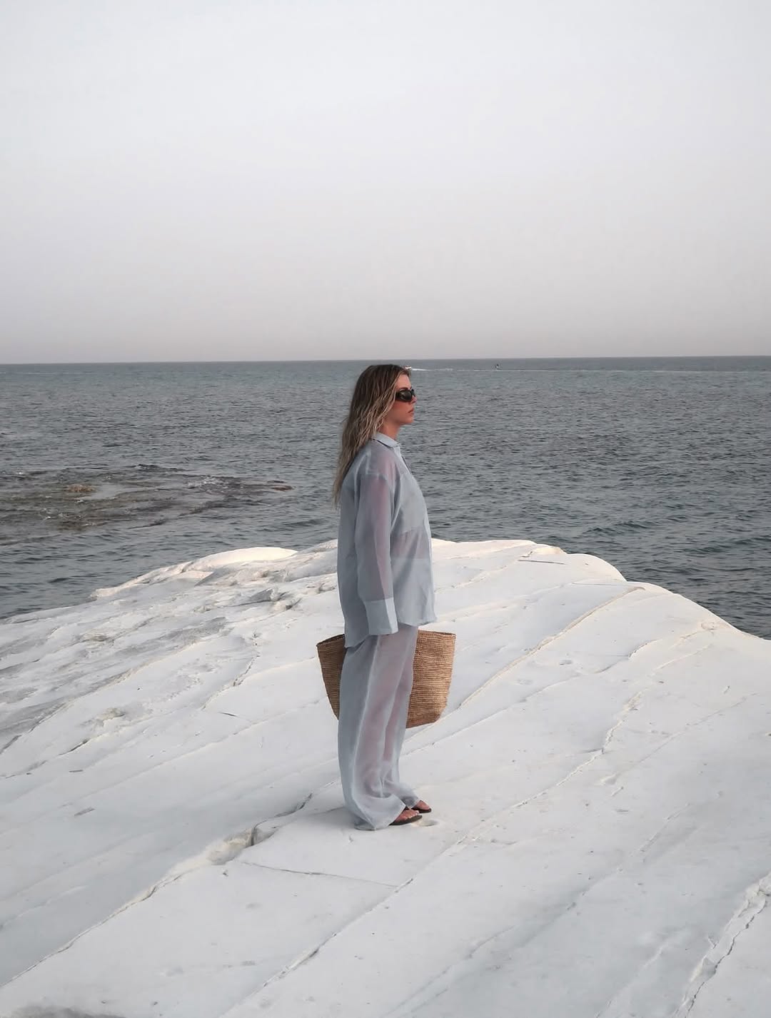 Side profile view of a model wearing a light blue sheer long-sleeve shirt and matching wide-leg trousers.