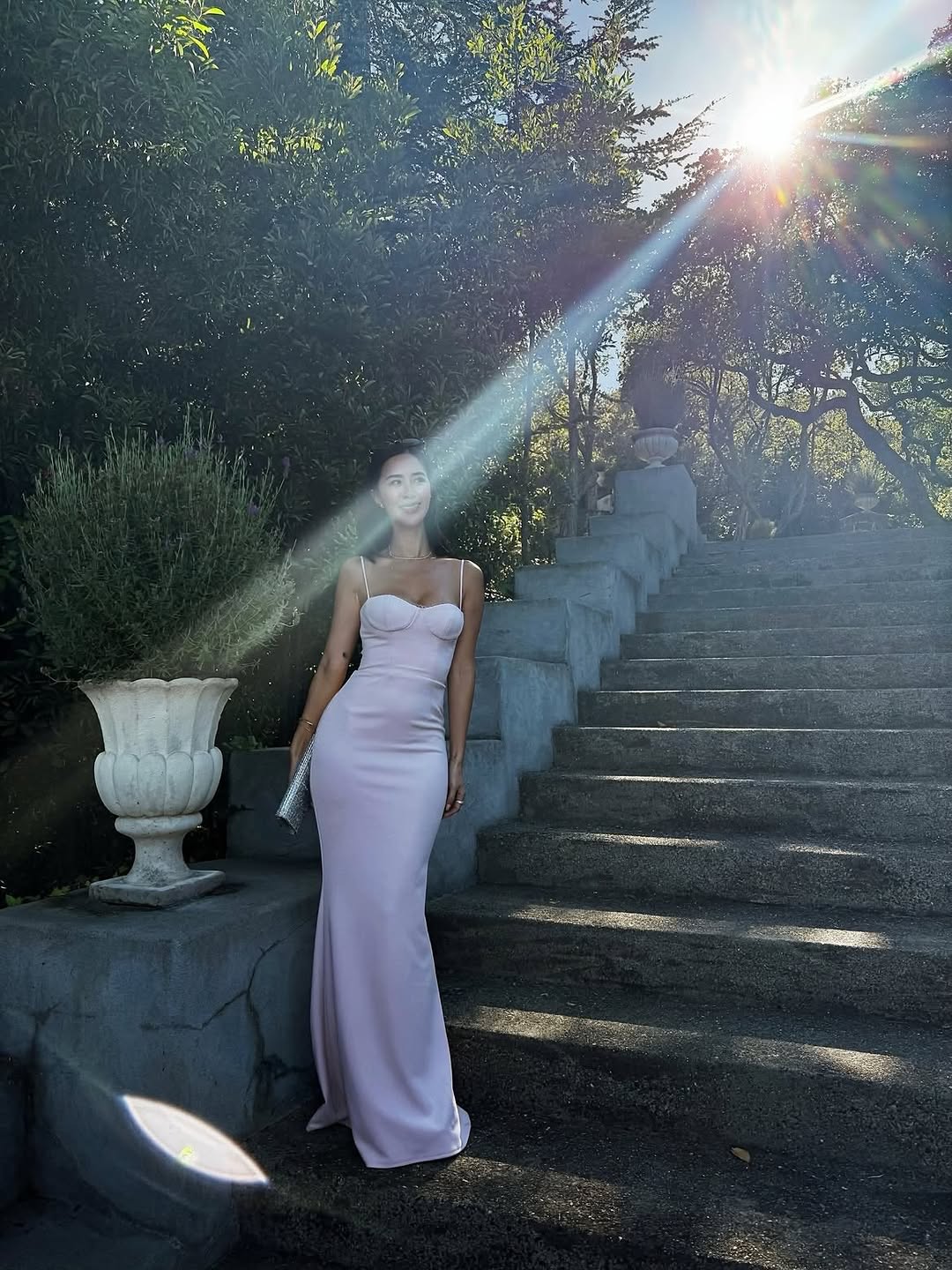 A floor-length, form-fitting gown in a pale pink or lilac shade. It features thin spaghetti straps and a structured bustier bodice with defined cups.