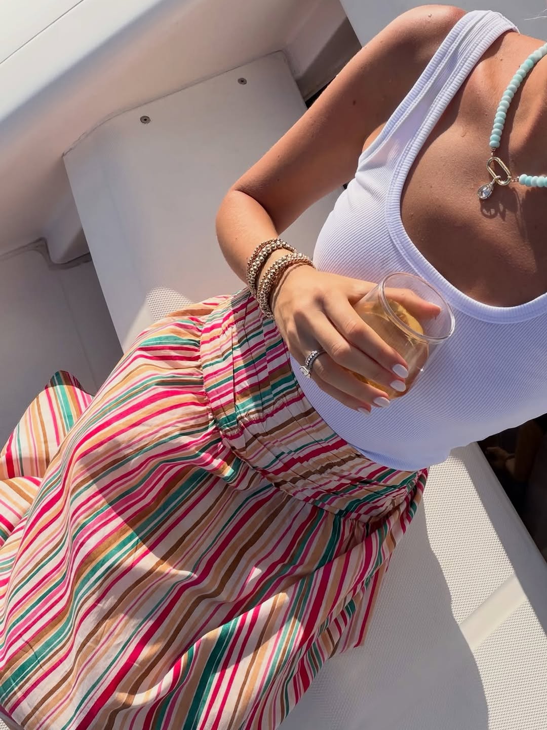 Close-up of a person wearing a white ribbed tank top and a colorful vertical-striped midi skirt.