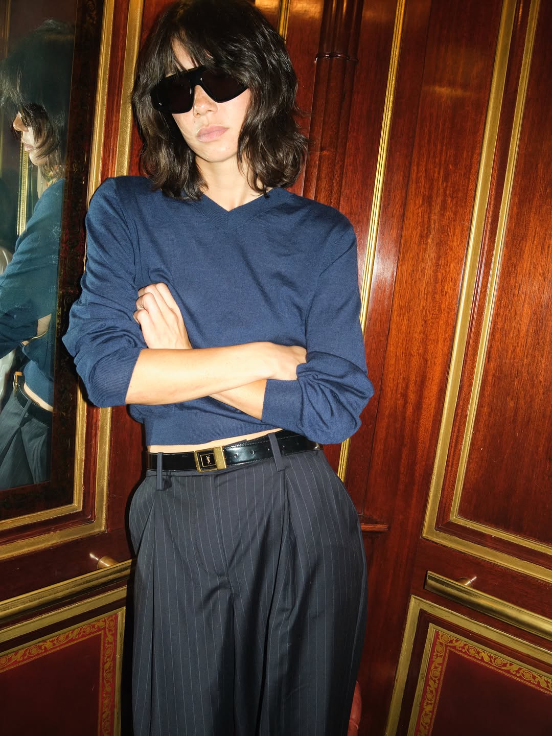 High-waisted, wide-leg trousers in a dark charcoal grey fabric with fine white pinstripes. Features deep front pleats and side pockets.