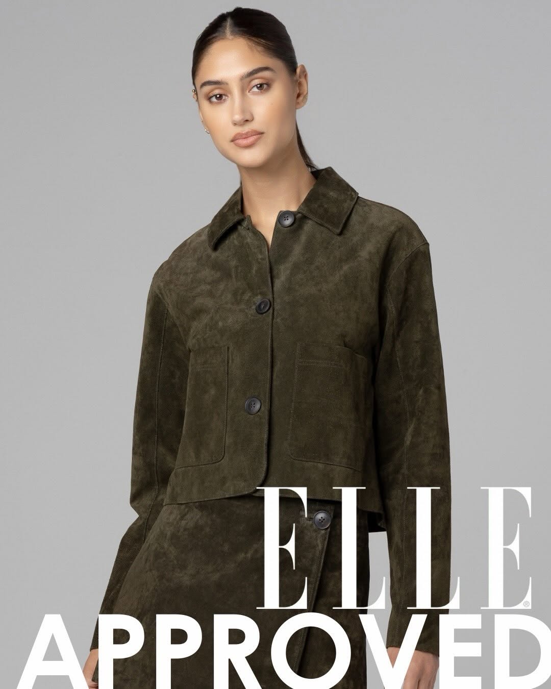 An olive green suede trucker-style jacket with a pointed collar, button-front closure featuring dark buttons, long sleeves, and two large patch pockets on the front.