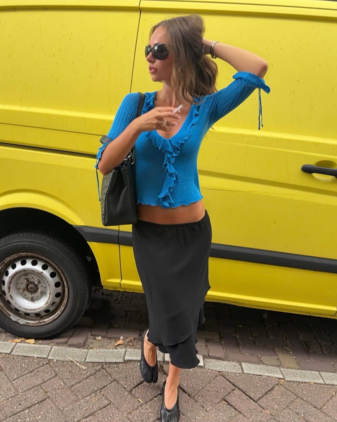 Bright blue ribbed knit crop top with V-neckline, ruffle trim along neckline and hem, three-quarter length sleeves with tie details at cuffs