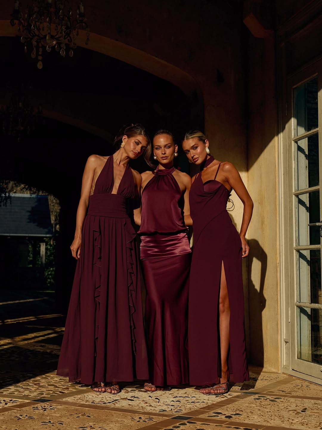 Deep plum floor-length halter gown with plunging V-neckline, wide waistband, and vertical ruffle details along the left side of the A-line skirt