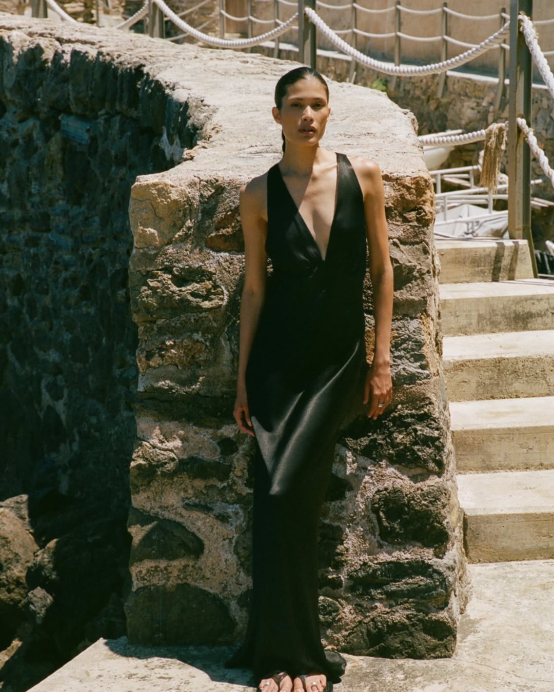 Front view of a model wearing a long black satin dress with a plunging neckline.