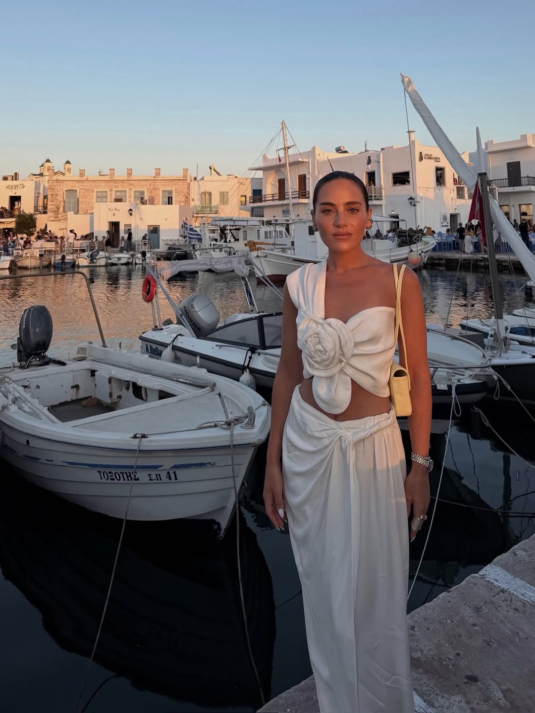 Front view of a woman in a white one-shoulder top with a large rosette detail and matching draped wide-leg trousers.