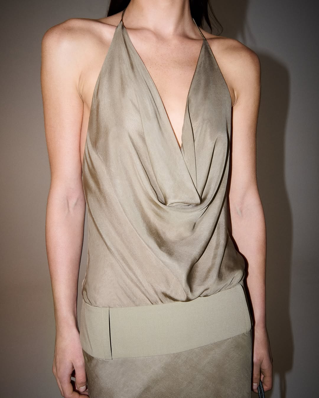 Close-up of the upper body showing a taupe silk-like halter top with a draped cowl neckline.