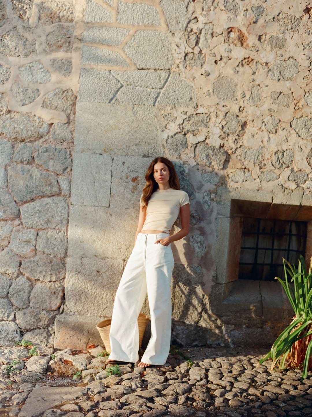 A model wearing a fitted cream short-sleeved t-shirt tucked into high-waisted white wide-leg jeans.