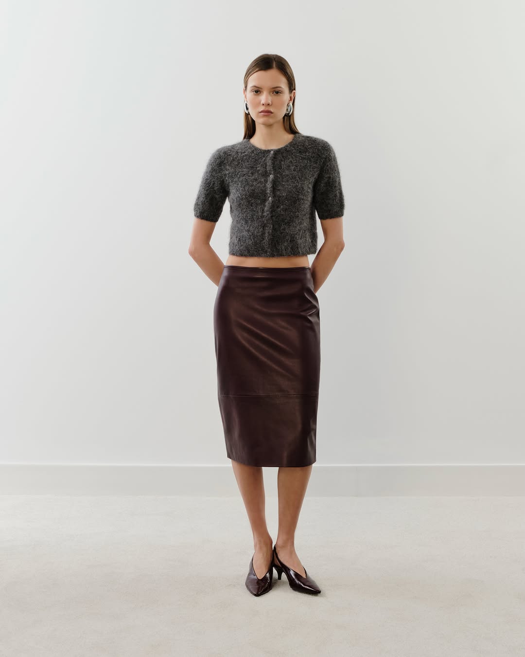 Full-body shot of a model wearing a fuzzy grey cropped cardigan and a dark brown midi skirt.