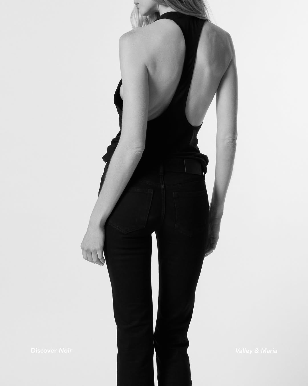 Rear view of model wearing the black open-back bodysuit paired with black jeans.