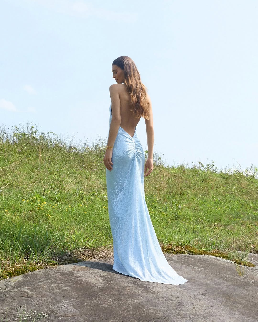 Rear view of a model wearing a floor-length light blue sequined gown with an open back.