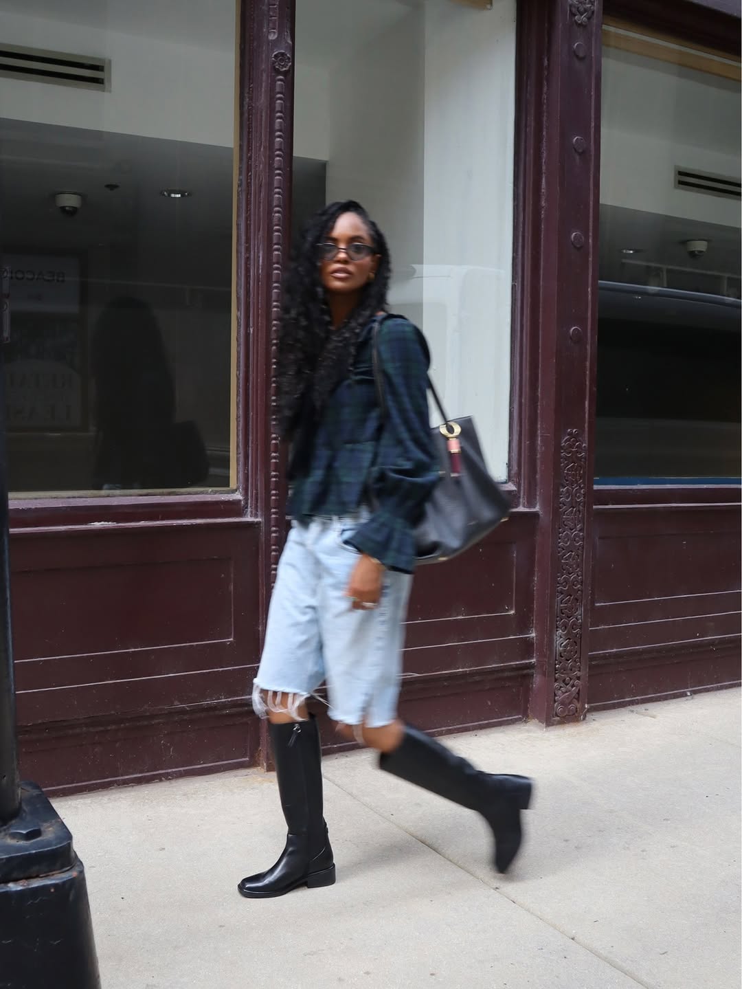 Model walking in a plaid peplum top, light wash denim shorts, and black knee-high boots.