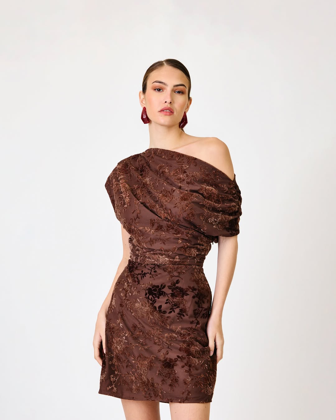 Close-up of a model wearing a chocolate brown, velvet-textured floral print one-shoulder mini dress.