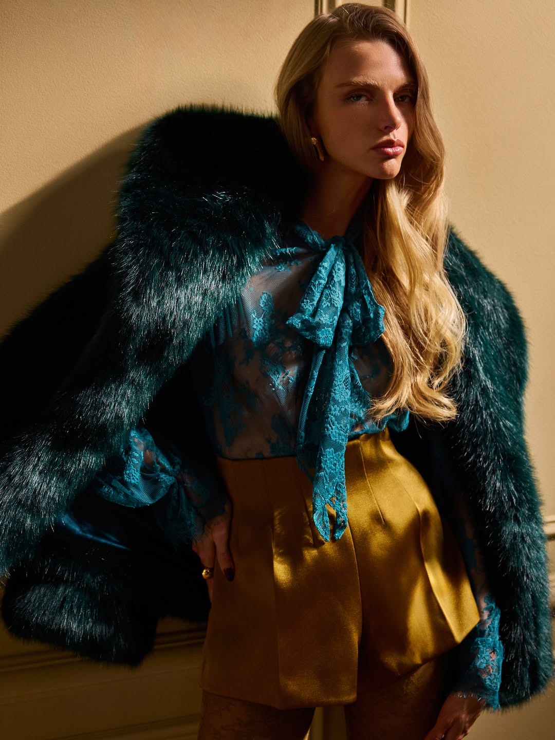 A dark emerald green faux fur coat with a plush texture, worn draped over the shoulders.