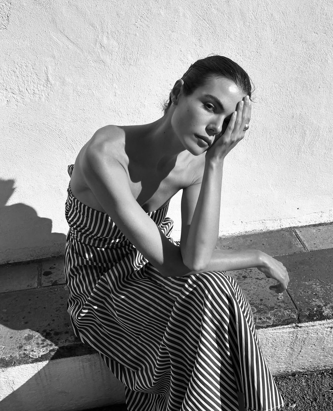 A strapless midi dress featuring a bold vertical stripe pattern in contrasting tones. The garment has a straight neckline and appears to be made of a lightweight fabric with…