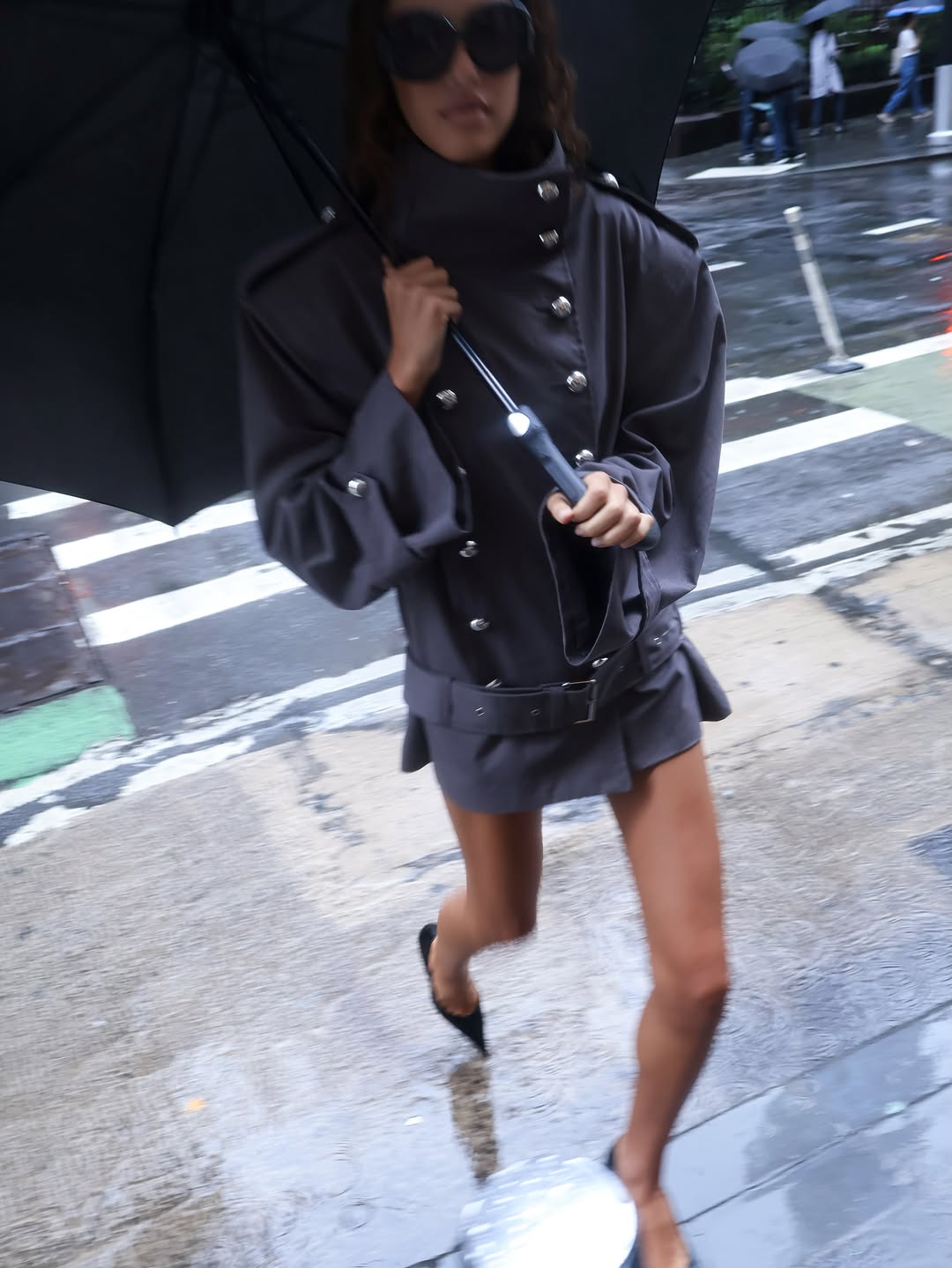 Model walking in rain wearing a grey double-breasted jacket and skirt set.