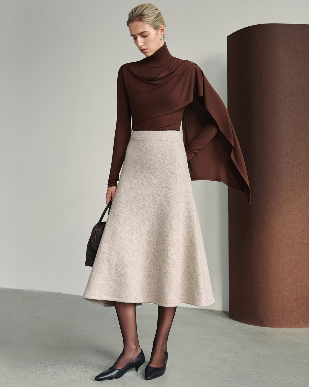 A dark brown, long-sleeved turtleneck top with a draped cowl neckline and an asymmetrical scarf-like extension falling from one shoulder.
